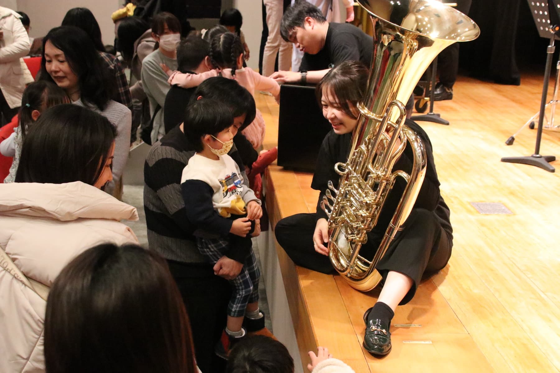楽器に触れて音を出してみる児童と、寄り添って教える演奏家（楽器体験の様子・イメージ）